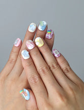 Hand model wearing short pastel press-on nails with 3D ice cream cones and gummy bear charms in pink and blue